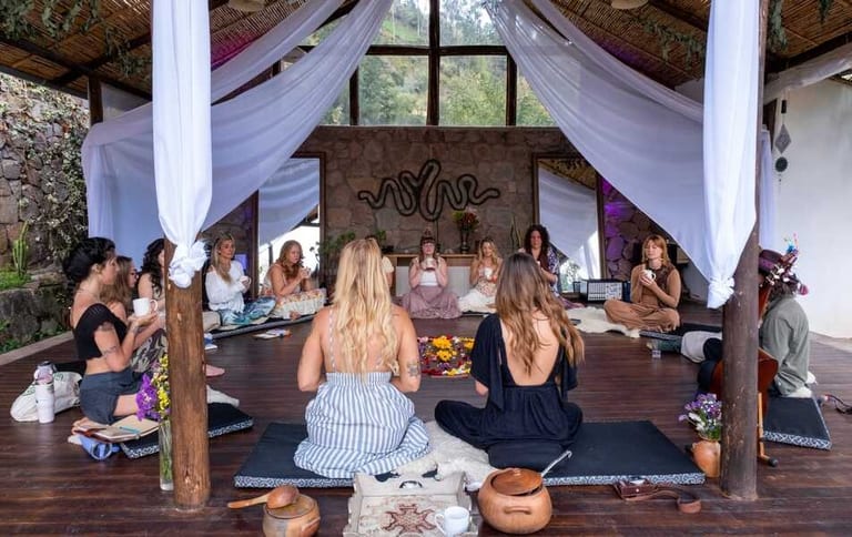 A group gathered in circle inside the Ayni temple, seated on cushions, with white curtains and an Andean stone altar behind them.