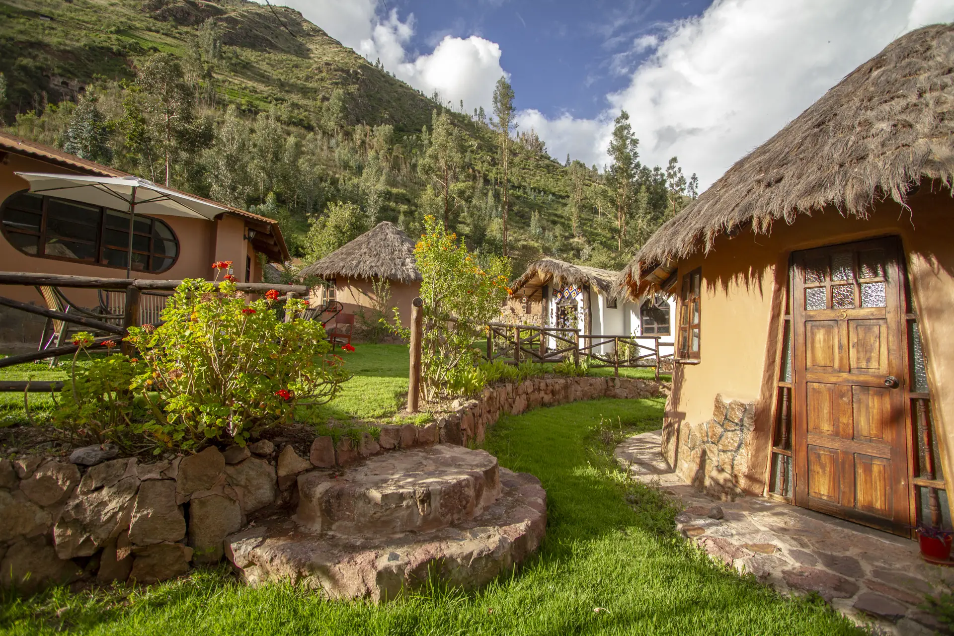 Adobe bungalows with thatched roofs along a stone path at Ayni Sanctuary, Sacred Valley